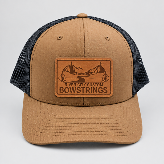 River City Custom Bowstrings trucker cap, tan crown with a charcoal mesh back and a leather patch of the bow mark